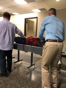Two men placing backpacks on conveyor belt for TSA inspection.
